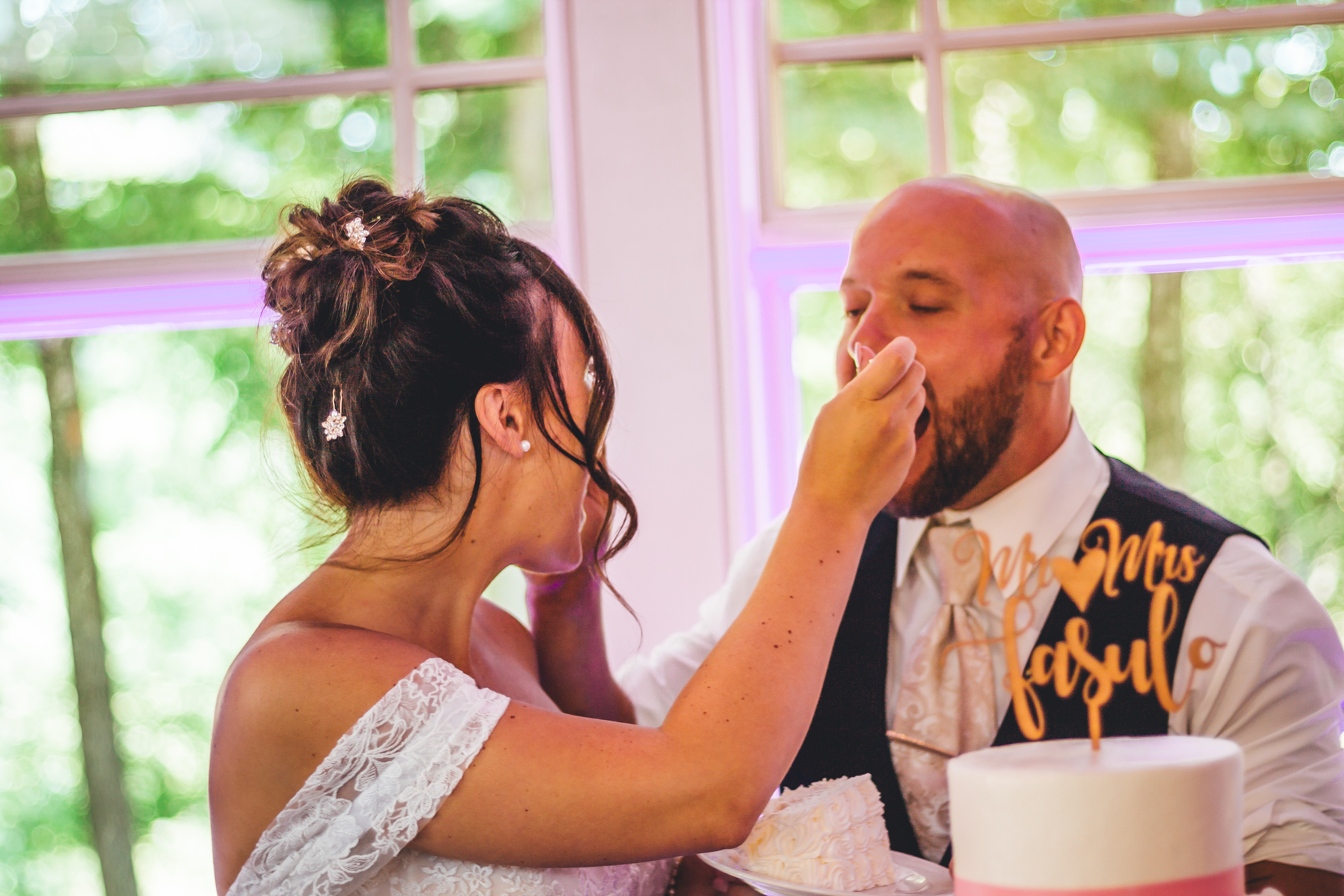 The groom covers his face emotionally as the bride, wearing a white lace strapless gown with an elegant updo adorned with hairpins, tenderly comforts him during