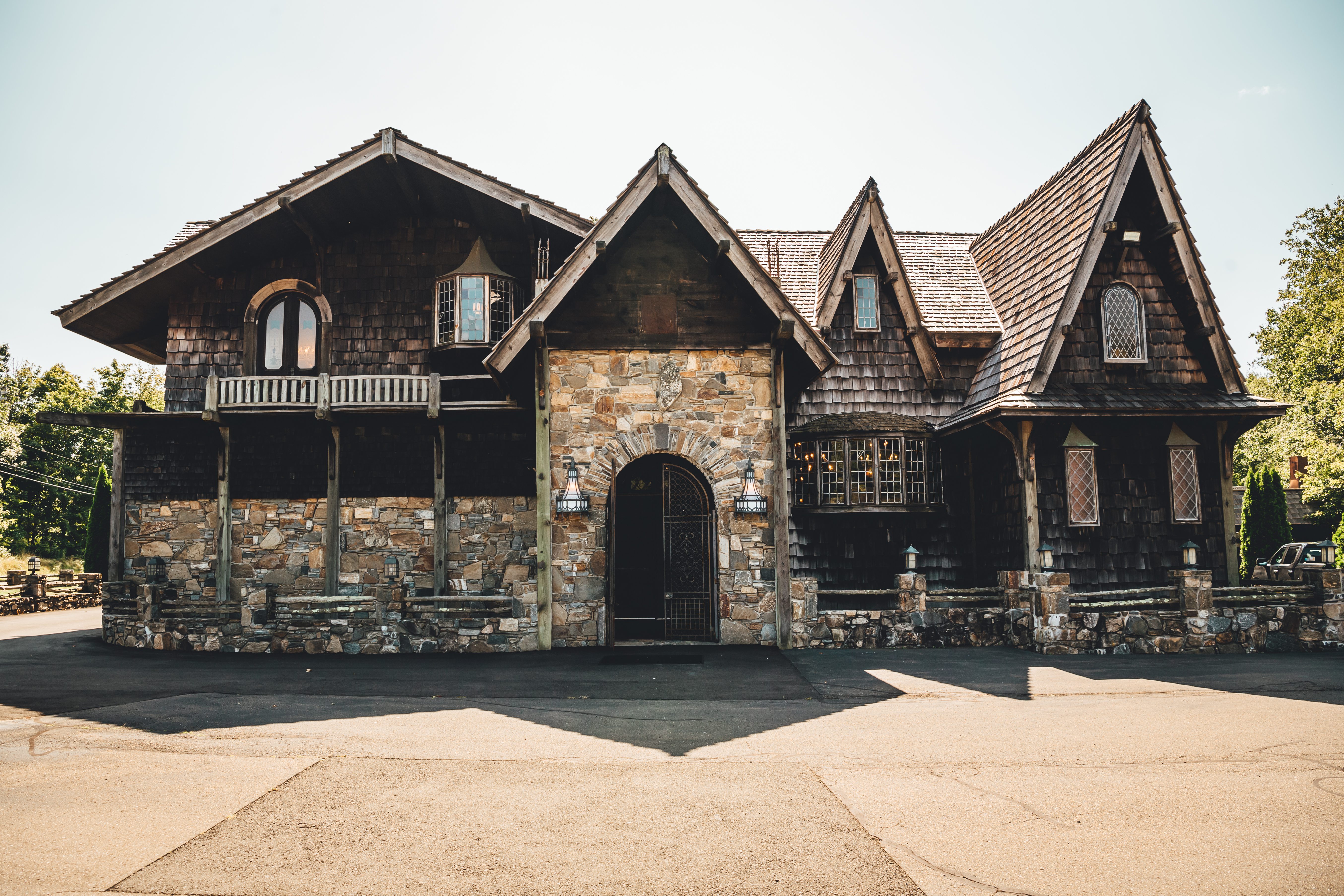 A striking dark stone and timber gothic-style venue building with multiple peaked roofs, arched doorway, and dramatic ar