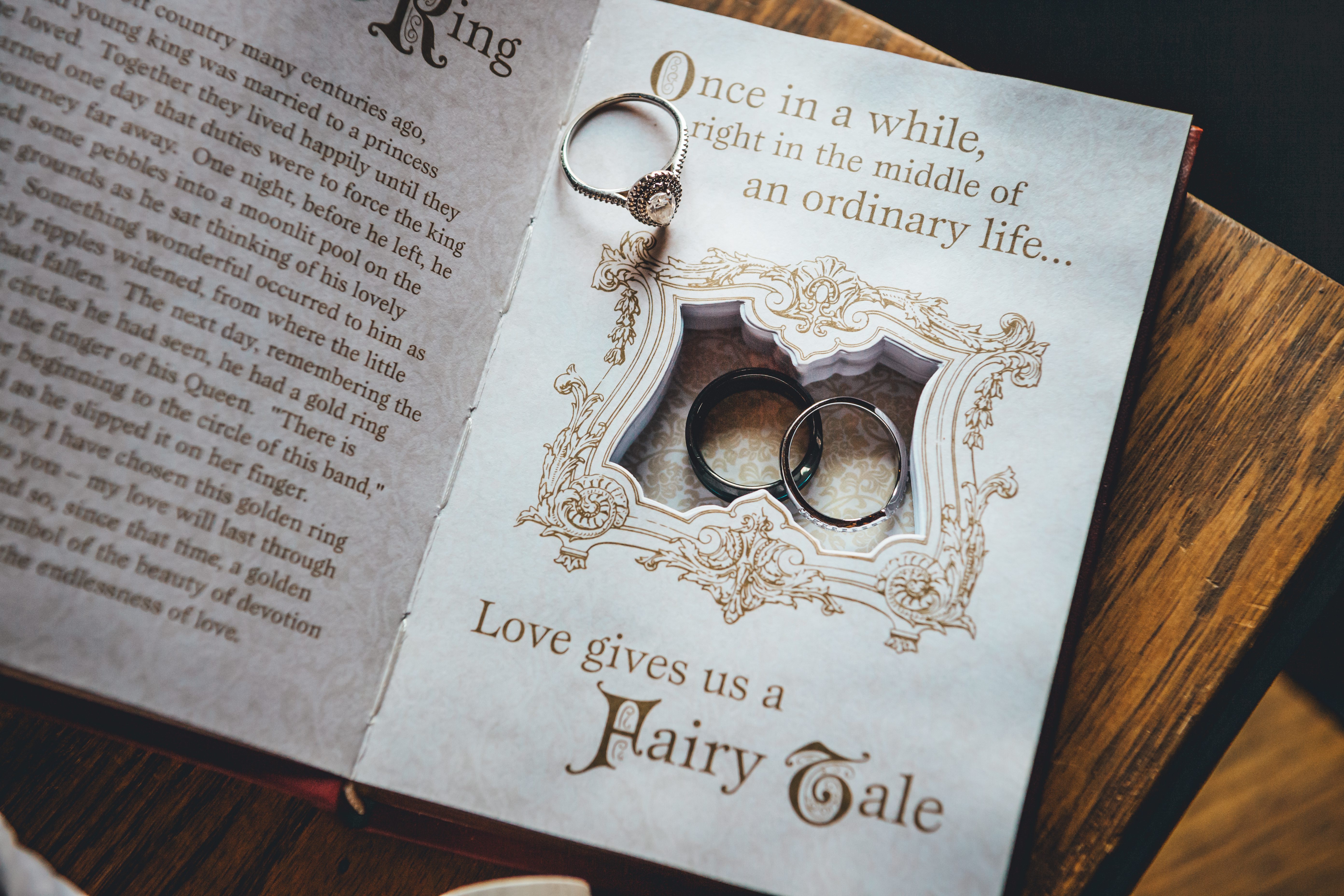 Wedding rings displayed on a fairy tale-themed ring holder book. The custom book features ornate gold filigree framing a