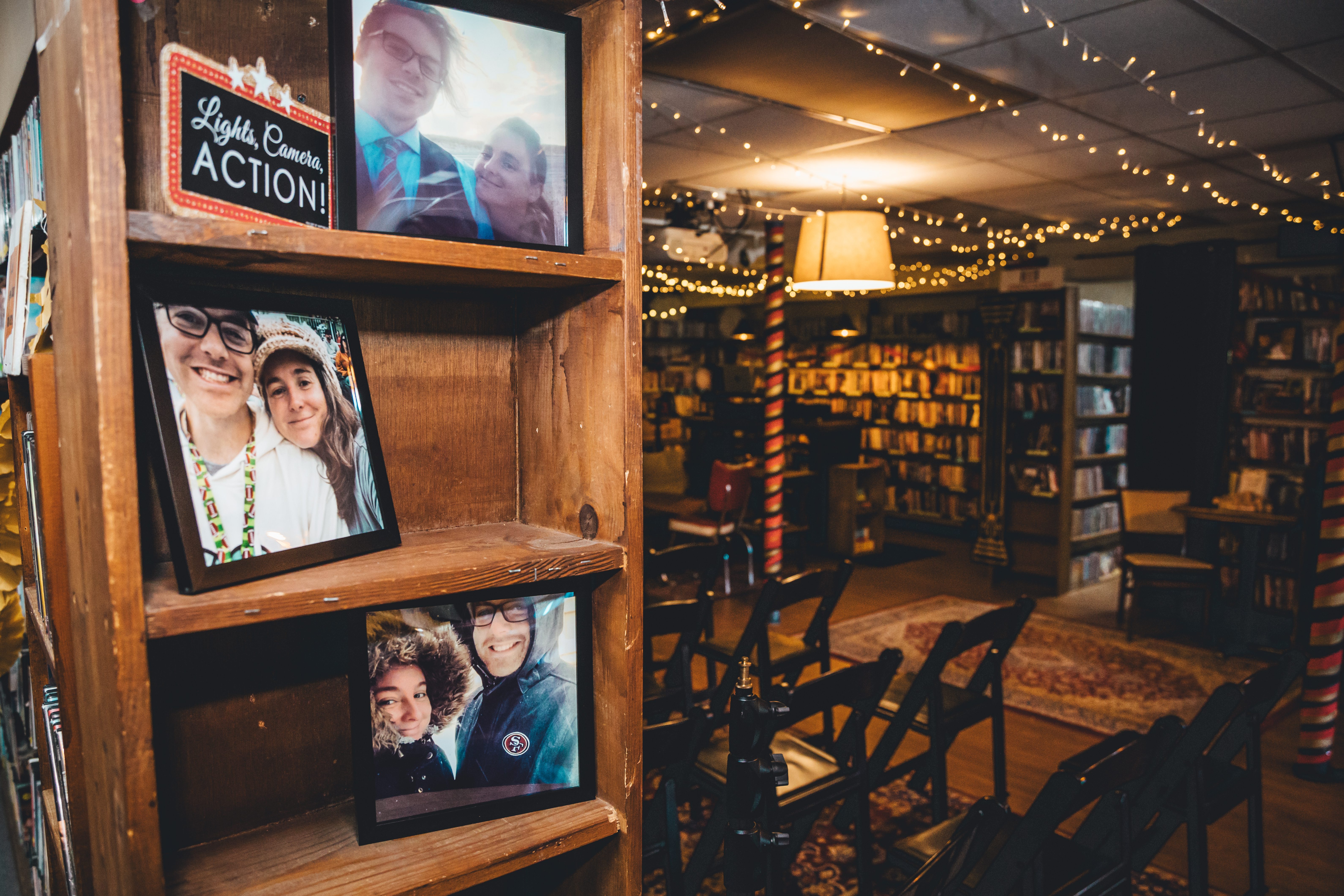 A wooden display shelf in a library-themed reception space showcases framed photos of the couple in various candid momen