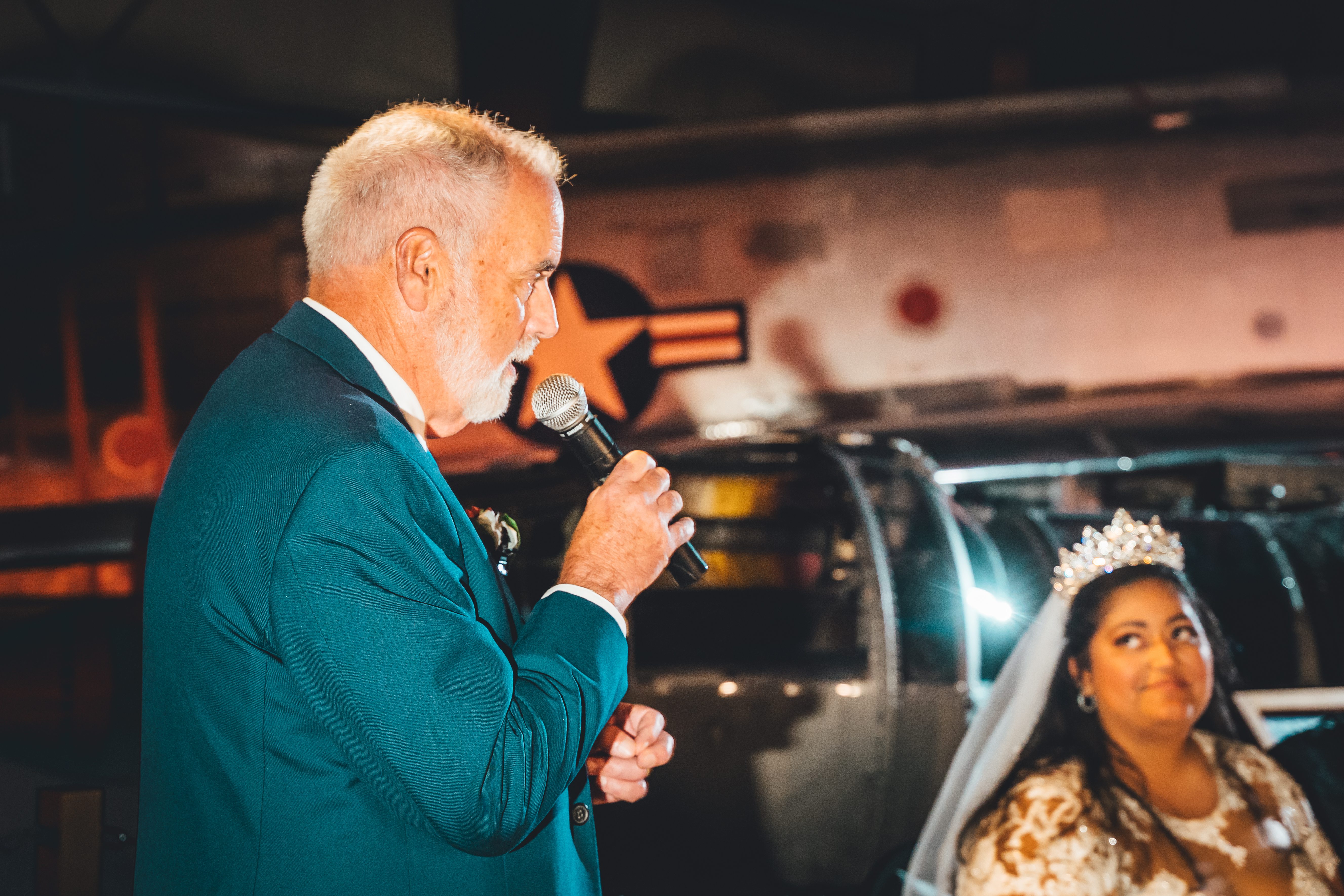 A wedding toast on the microphone in front of a vintage aircraft