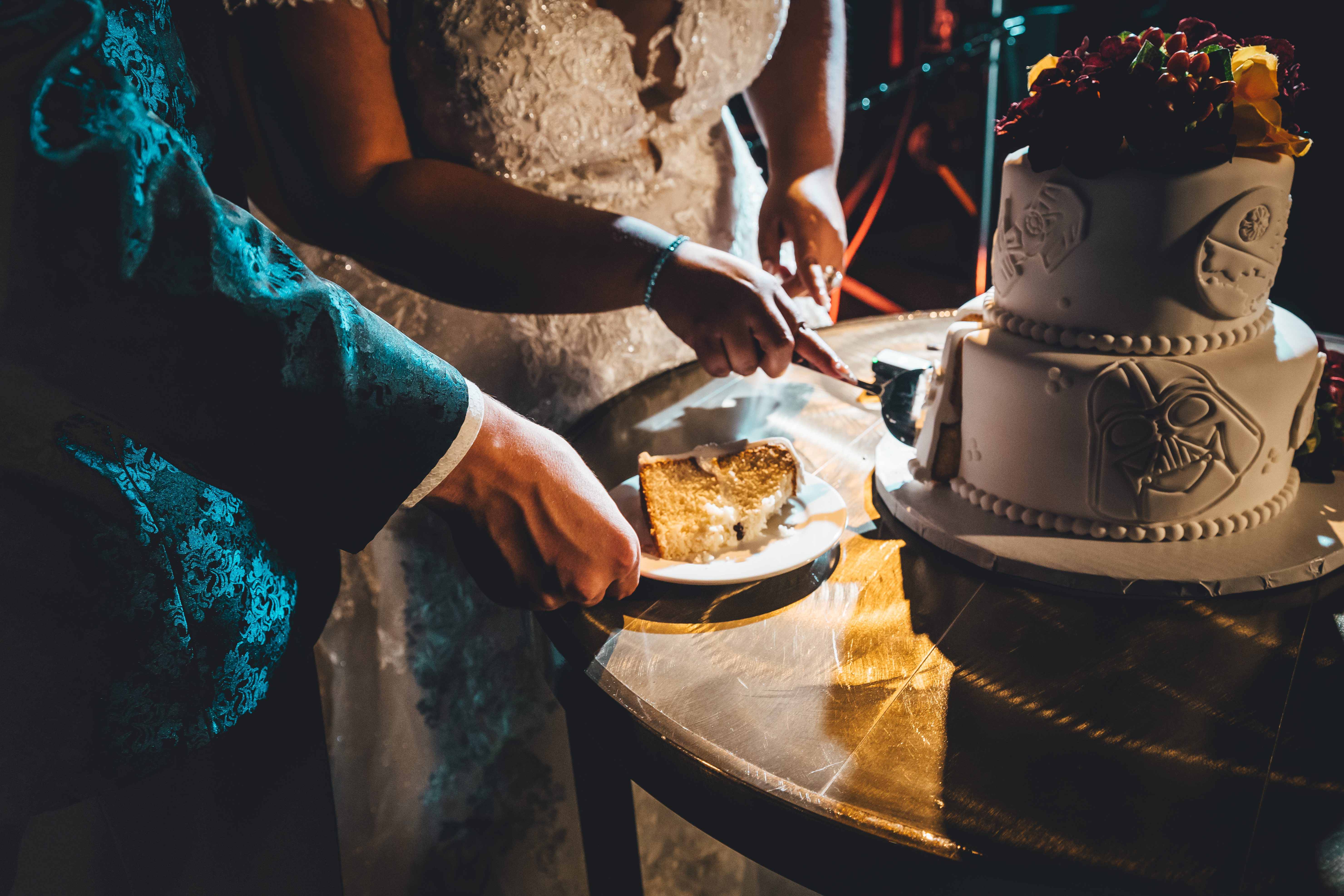 The couple cuts their wedding cake together, which features Star Wars-themed decorations including Darth Vader and Yoda face designs on white fondant tiers with