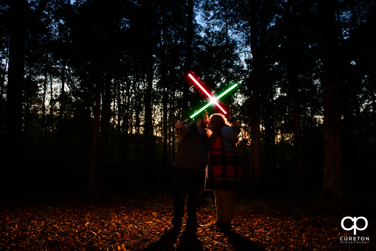A couple crosses red and green lightsabers in an X above their heads at dusk