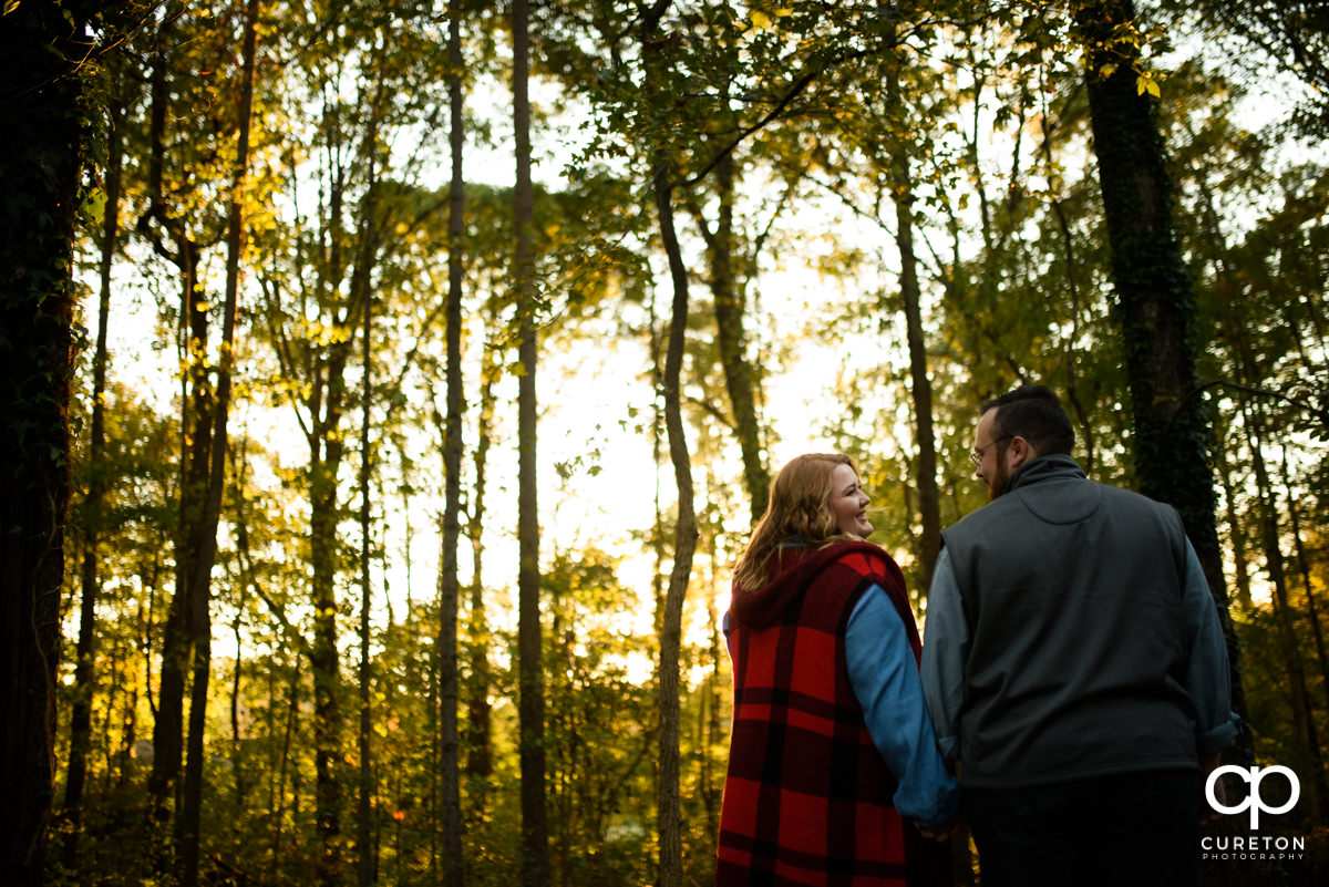 An engaged couple walks hand in hand through a sunlit autumn forest
